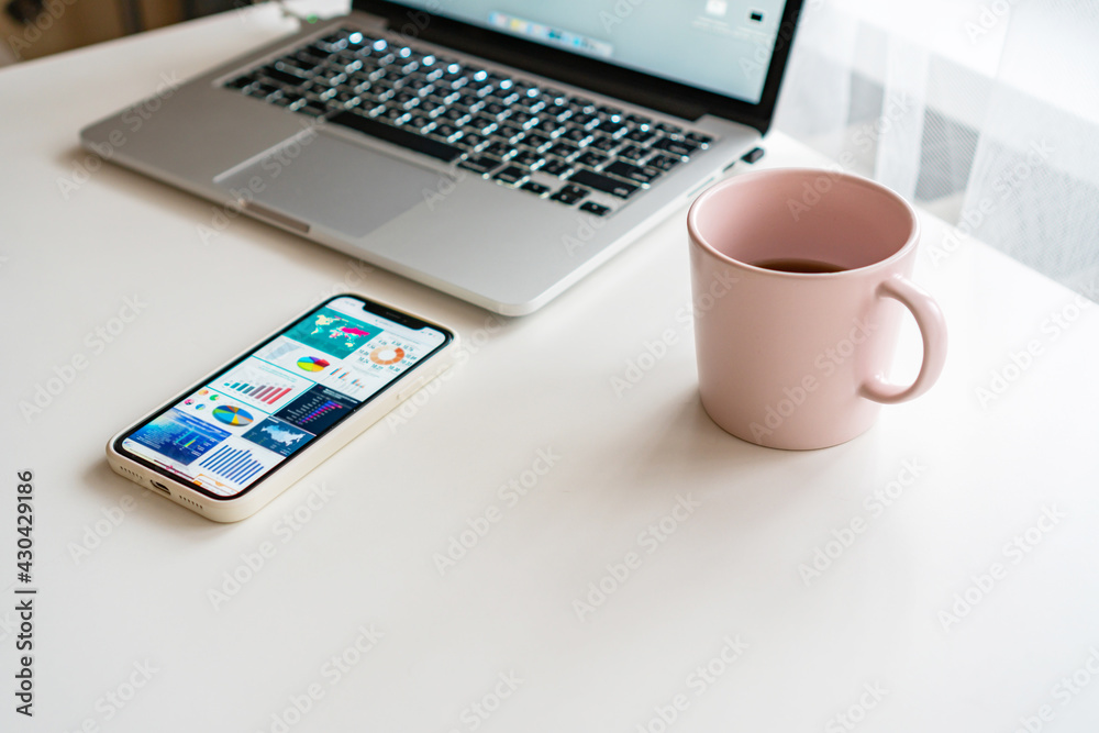 there is a pink mug and a laptop on the table, a mobile phone is nearby there is a pink mug and a laptop on the table, a mobile phone is nearby