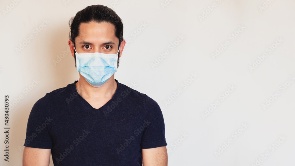 Young latin man wearing a face mask for safety from COVID-19 on a clear background with copy space Young latin man wearing a face mask for safety from COVID-19 on a clear background with copy space