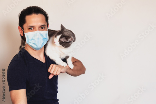 Young latin man with a cat on his shoulders wearing a face mask for safety from COVID-19 on a clear background with copy space © Angel Gruber