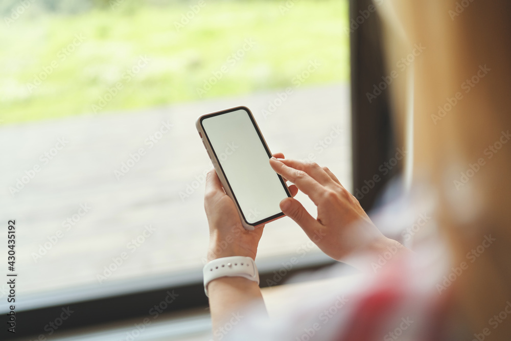 Side view of young girl holding a black smartphone while standing near the window