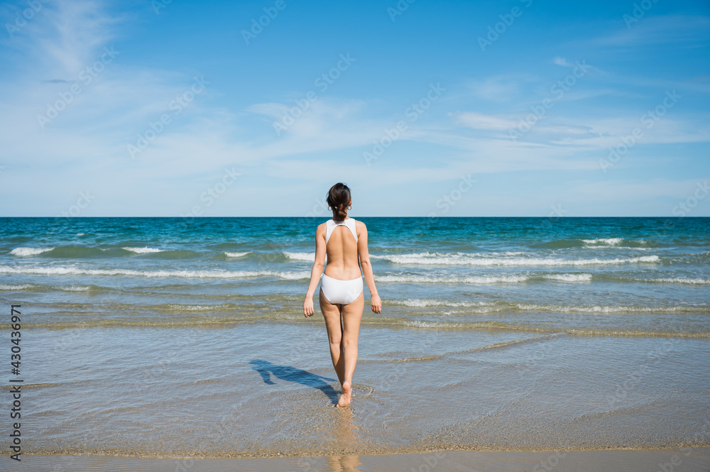 Attractive young asian woman in swimwear walking on the beach at tropical sea in sunny day Attractive young asian woman in swimwear walking on the beach at tropical sea in sunny day