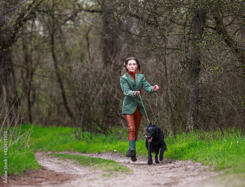 Young lady in country style fashionable clothes walking with hunting dog along the spring forest path