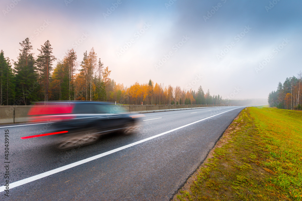 Suburban autumn highway. Coniferous forest in the fog. The car goes on the road. Autumn morning. View from the side of the road. Russia, Europe. Beautiful nature.