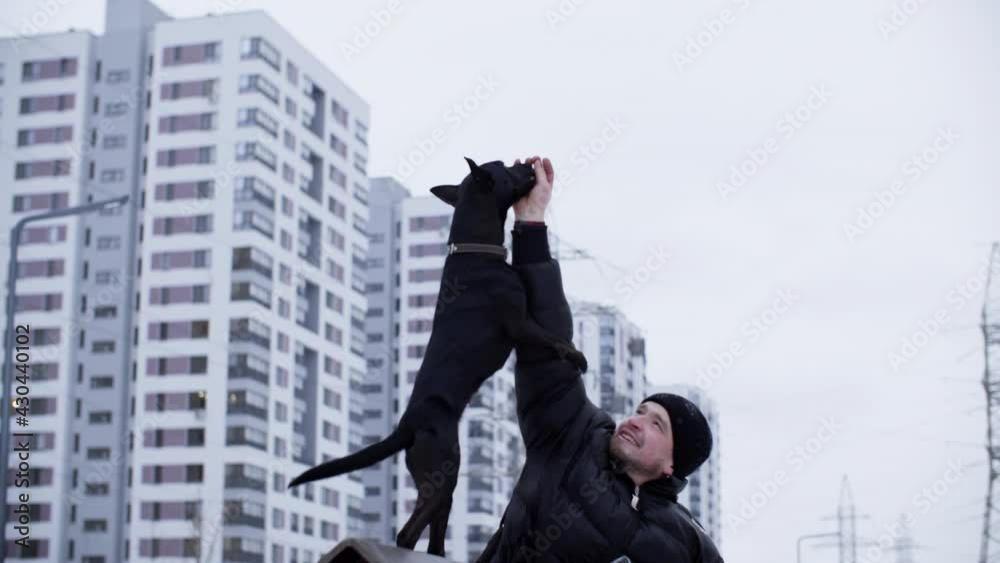 Man handler training black dog to stand on its hind legs on winter walk. Black dog training with owner on city walk in winter Man handler training black dog to stand on its hind legs on winter walk. Black dog training with owner on city walk in winter
