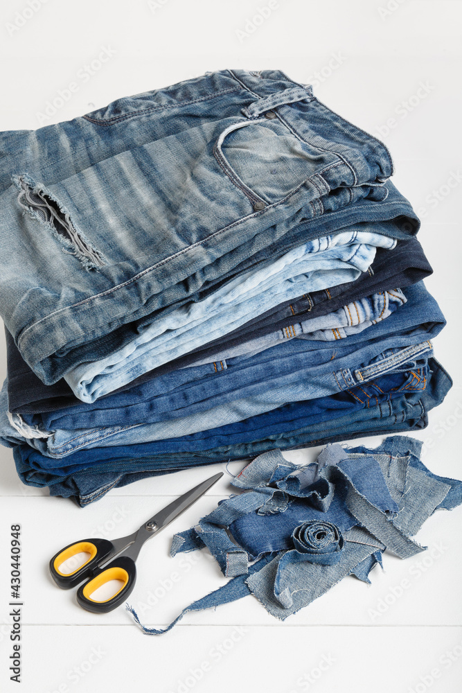 Stockfoto Upcycle old denim garbage. Recycling old jeans. Stack of old blue  jeans, cut pieces ready for recycling and scissors on white background.  Circular economy. Pile of discarded old blue jeans. Zero