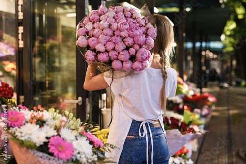 Vrouw bloemist met een hoop roze pioen bloemen in haar kleine bloemenwinkel