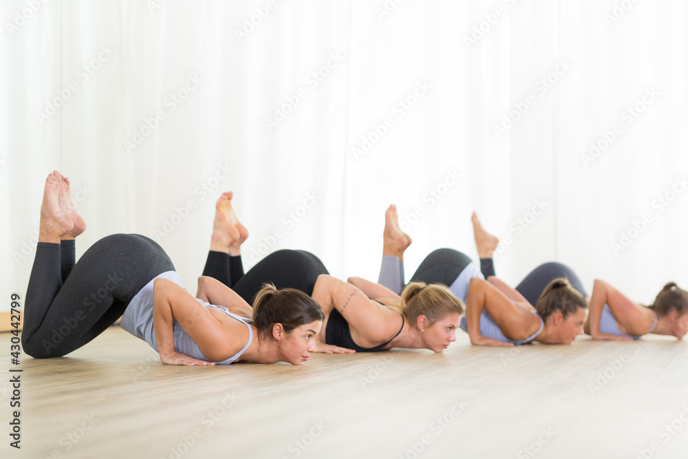 Obraz premium Group of young sporty sexy women in yoga studio, practicing yoga lesson with instructor, forming a line in Shishosana bent puppy dog asana pose. Healthy active lifestyle, working out indoors in gym