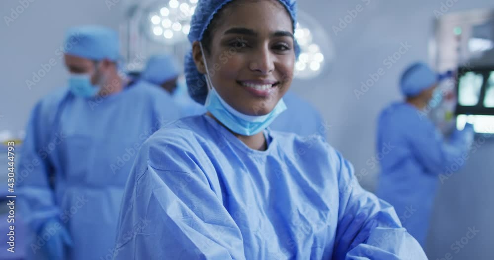 Portrait of mixed race female doctor standing in operating theatre smiling to camera