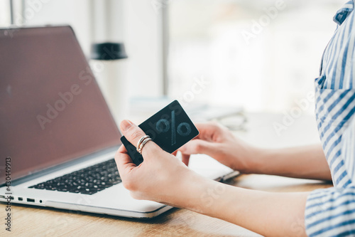 Woman enters promocode from discount card on website sitting at wooden table with laptop. photo