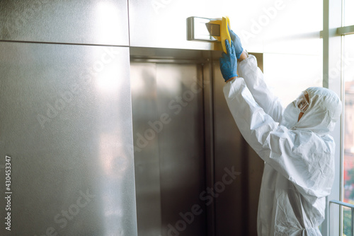 Cleaning and disinfection of the elevator to prevent COVID-19. Worker wearing protective suit sprays disinfectant buttons of the lift.  © maxbelchenko
