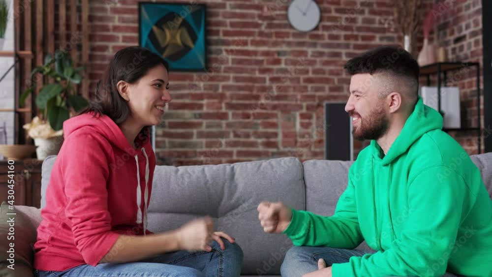 Young couple plays in rock paper scissors on sofa having fun freetime together enjoying each other company. Teenager friends sitting and play funny hand game, together in modern room in apartment.