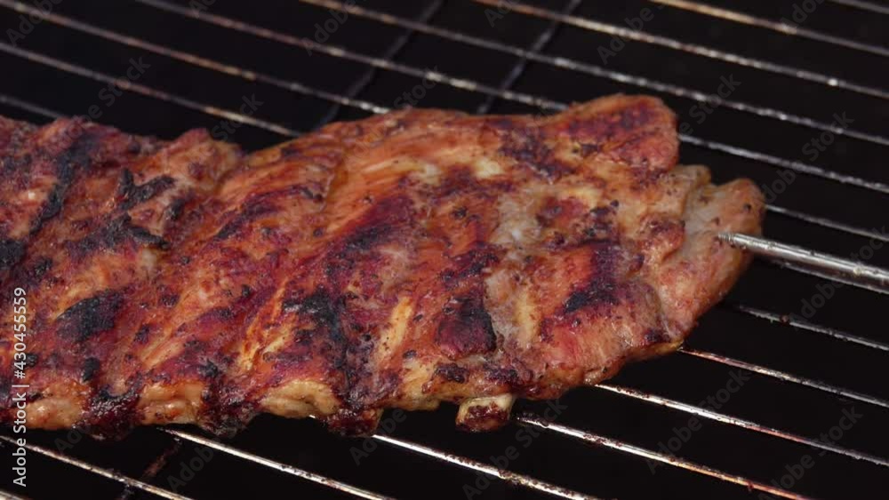 Close-up of the appetizing crunchy ribs rotated on the grill grid on the background of the open fire Close-up of the appetizing crunchy ribs rotated on the grill grid on the background of the open fire