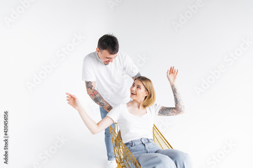 Man carries a woman in a shopping cart on a white background. Cheerful young couple