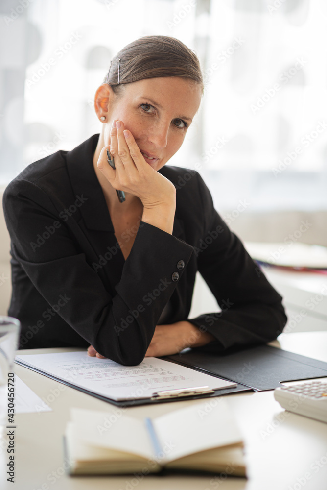 Young businesswoman sitting at her office desk with reports and paperwork in front of her Young businesswoman sitting at her office desk with reports and paperwork in front of her
