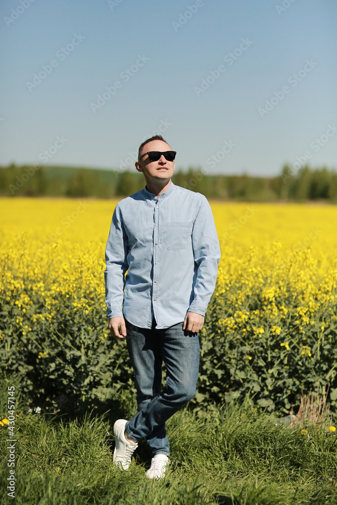 A young man in sunglasses is walking and having fun through a Sunny yellow rapeseed field, the concept of travel and freedom. summer holiday background