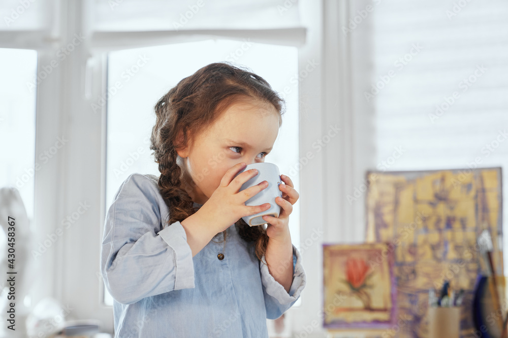 Cute thirsty girl is drinking water from the cup. Small schoolgirl having fresh beverage. Tasty drinking. High quality image Cute thirsty girl is drinking water from the cup. Small schoolgirl having fresh beverage. Tasty drinking. High quality image