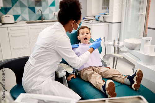 Black female dentist examining boy s teeth during appointment at dentist s office.