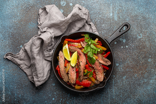 Traditional Mexican dish Beef fajitas with bell peppers in black cast iron pan on rustic stone background from above, American Mexican food 