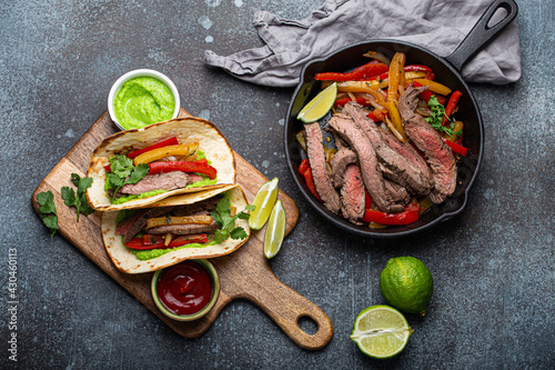 Process of making traditional Mexican dish Beef fajitas tacos served on wooden cutting board with tomato salsa and guacamole on rustic stone background from above, American Mexican food  photo