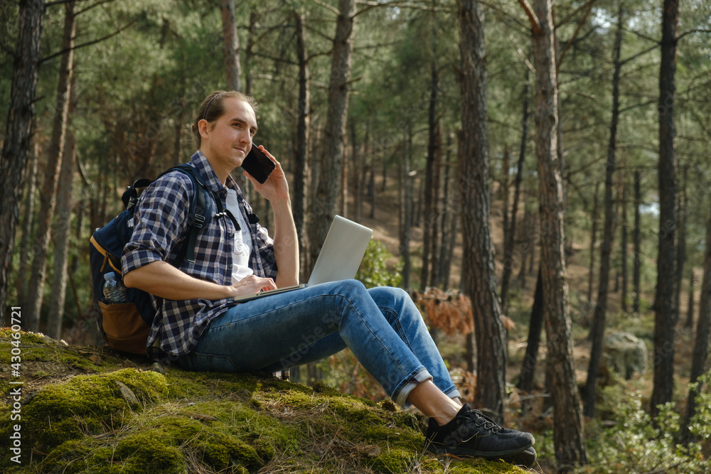 Man sitting on ground at forest talking on smartphone and working on laptop Man sitting on ground at forest talking on smartphone and working on laptop