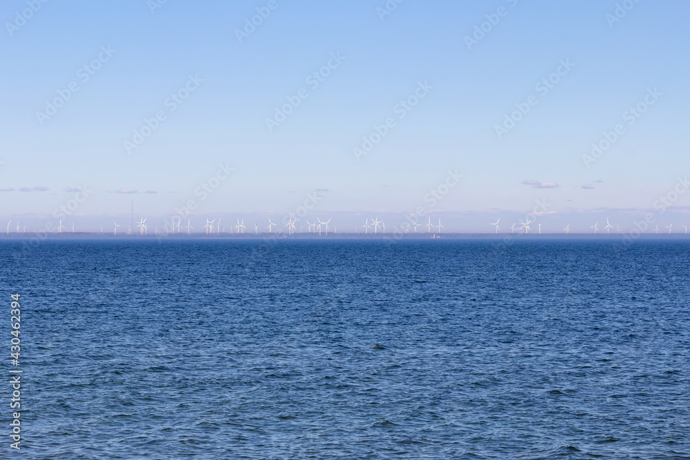 A view from open water of a wind turbine farm on the far shore as seen from a ferry - light hazy blue sky over dark blue water