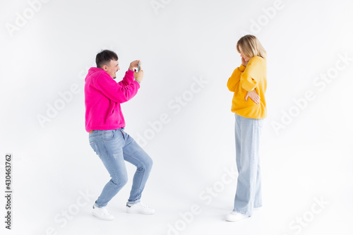 Image of a man take photo of his positive optimistic woman on white background by mobile phone.