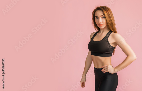 Fototapeta Naklejka Na Ścianę i Meble -  Fitness girl smiling in black sportswear on a pink background. Slim woman with a beautiful athletic body and tanned skin