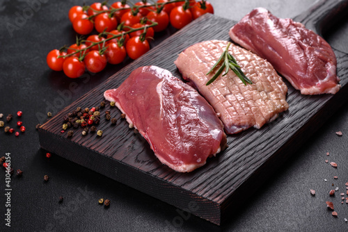 Raw duck breast with herbs and spices on a dark concrete background