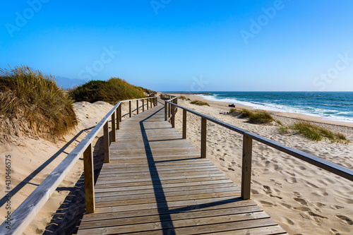 Wooden path at Costa Nova d'Aveiro, Portugal, over sand dunes with ocean view, summer evening. Wooden footbridge of Costa Nova beach in a sunny day. Aveiro, Portugal.