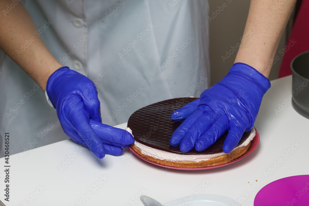A woman prepares a marshmallow cake. Places a layer of jelly and marshmallows on the biscuit. Works with a mask and gloves.