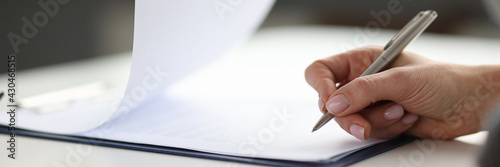 Woman writing with ballpoint pen in documents on clipboard in office closeup