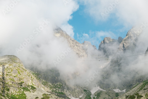 Panoramic view of rocky mountains covered with fluffy clouds. 