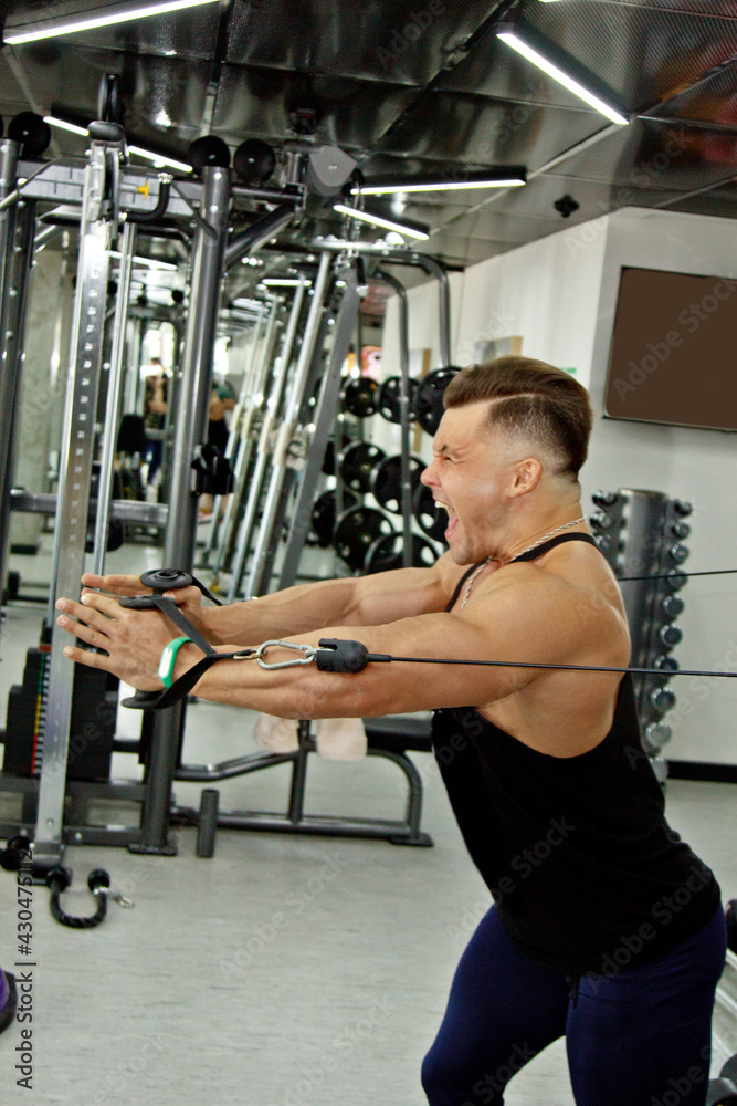 a man with big muscles is engaged in weightlifting in the gym. A pumped-up athlete goes in for sports on heavy weight simulators. sport exercises. Vivid emotions of work on the face a man with big muscles is engaged in weightlifting in the gym. A pumped-up athlete goes in for sports on heavy weight simulators. sport exercises. Vivid emotions of work on the face