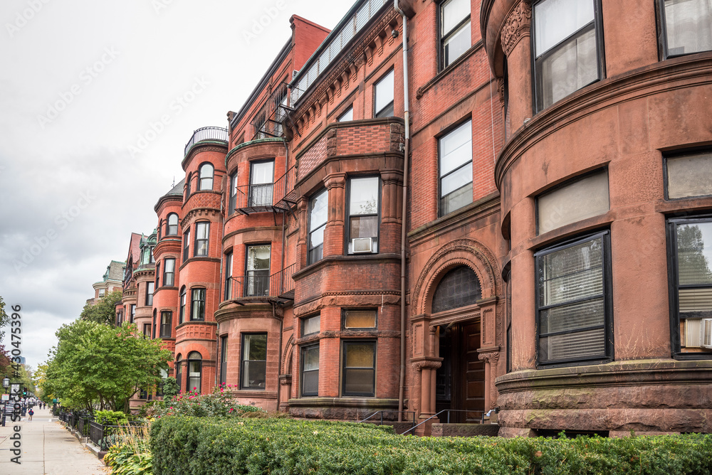 Row of historic red-brick townhouses with fenced front yards on an overcast autumn day