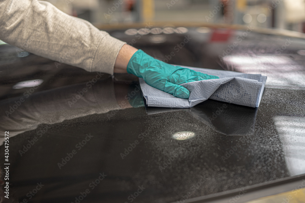 worker with gloves cleaning canopy glass in automotive plant