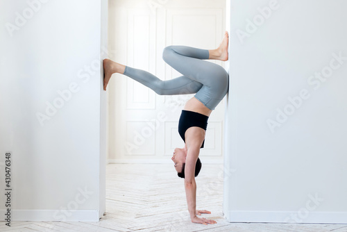 A young woman practices yoga and stands on her arms in the arch of a bright room. Young attractive yogi woman practicing yoga concept