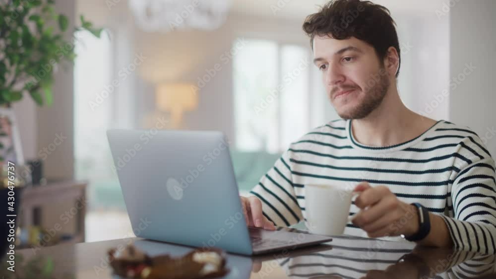 Handsome Adult Man Using Laptop Computer, Sitting in Living Room and Drinking Tea or Coffee in Apartment. Attractive Man is Online Shopping on Internet, Watching Funny Videos on Streaming Service. Handsome Adult Man Using Laptop Computer, Sitting in Living Room and Drinking Tea or Coffee in Apartment. Attractive Man is Online Shopping on Internet, Watching Funny Videos on Streaming Service.