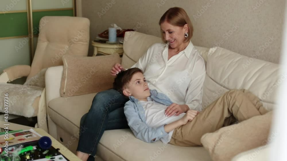 Teenager lies on the lap of an adult woman, she strokes his head. Teenager lies on the lap of an adult woman, she strokes his head.