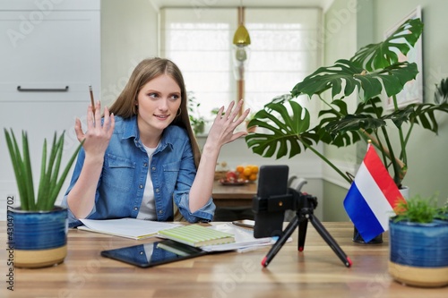 Female student sitting at home studying online, looking at smartphone webcam