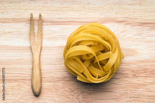 Italian pasta next to the wooden fork on wooden surface.