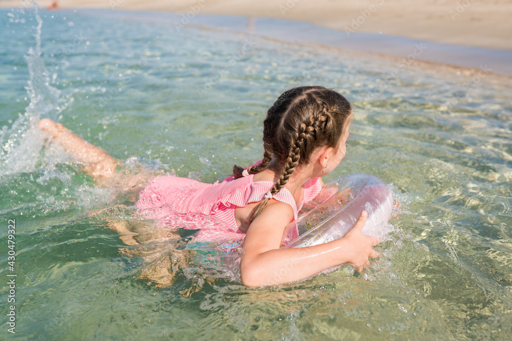 Happy child girl with inflatable ring learning to swim in sea on sunny day. Fun water toys for kids. Family summer holidays on beach concept. Happy child girl with inflatable ring learning to swim in sea on sunny day. Fun water toys for kids. Family summer holidays on beach concept.