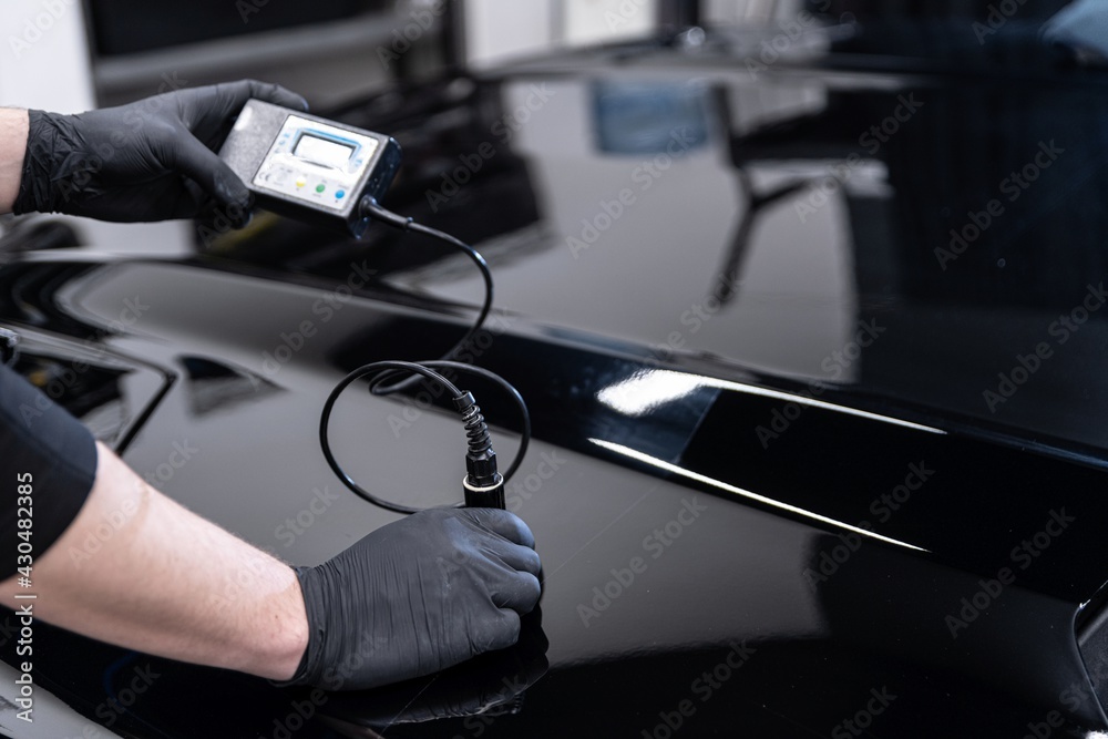 Man mechanic in car service checking varnish thickness with electronic sensor