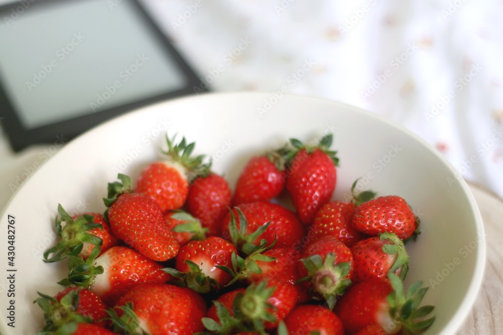Bowl of strawberries and e-reader on a bed. Selective focus. Bowl of strawberries and e-reader on a bed. Selective focus.