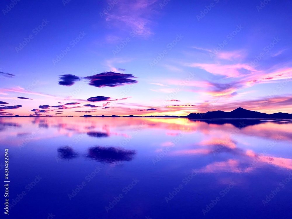 Sunset over lake. Wonderful sunset in mountains. Surreal natural landscape at salt flat Salar de Uyuni. Bright colors of desert. Incredible sky clouds reflection in calm water. Magical alien nature.