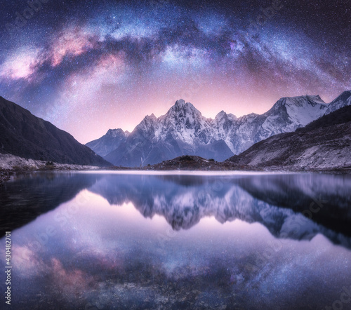 Milky Way over snowy mountains and lake at night. Landscape with snow covered high rocks, purple starry sky, reflection in water in Nepal. Sky with stars. Amazing bright milky way in Himalayas. Space 
