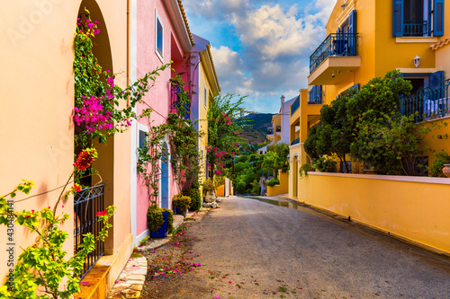 Fototapeta Naklejka Na Ścianę i Meble -  Traditional street with greek houses with flowers in Assos, Kefalonia island. Traditional colorful greek houses in Assos village. Blooming fuchsia plant flowers. Kefalonia island, Greece