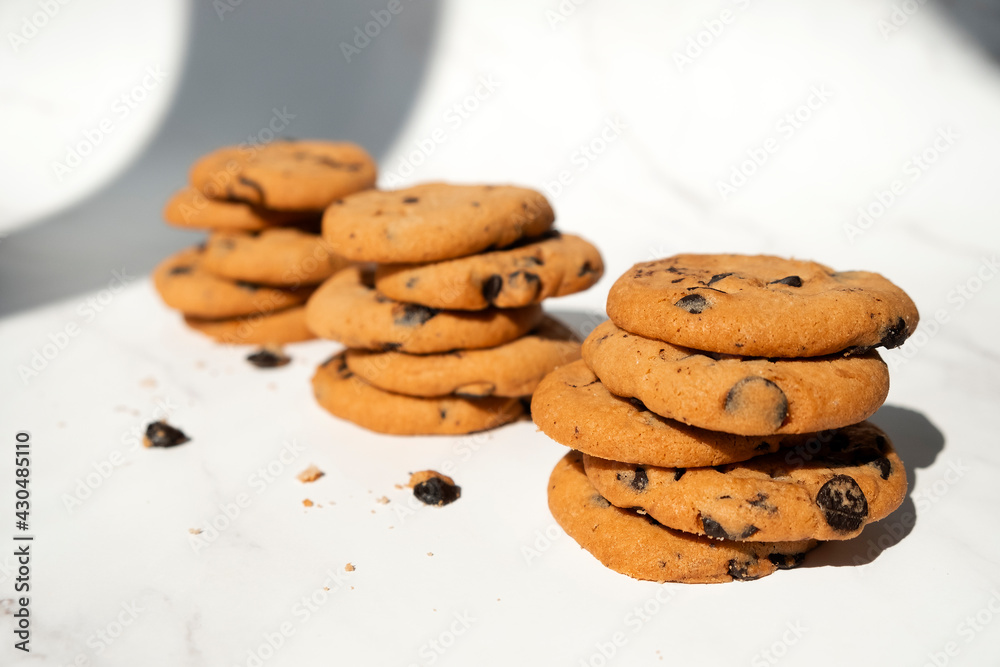 Stacks of chocolate chip cookies with pieces of chocolate in sun light with shadows. Recipe of oatmeal biscuits with chocolate chips. Homemade bakery. Stacks of chocolate chip cookies with pieces of chocolate in sun light with shadows. Recipe of oatmeal biscuits with chocolate chips. Homemade bakery.