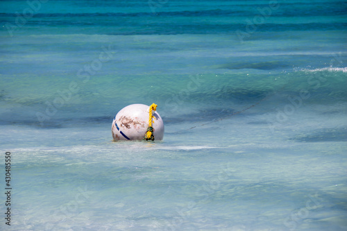A round white buoy with a blue stripe and a yellow rope attached bobs up and down in small waves in Carlisle Bay, Barbados, one of the most popular snorkelling spots on the island.