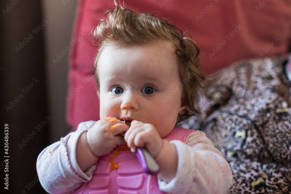 Portrait of a little blond toddler girl. Spoon eating. Dirty mouth. Mom feeds the baby. Portrait of a little blond toddler girl. Spoon eating. Dirty mouth. Mom feeds the baby.