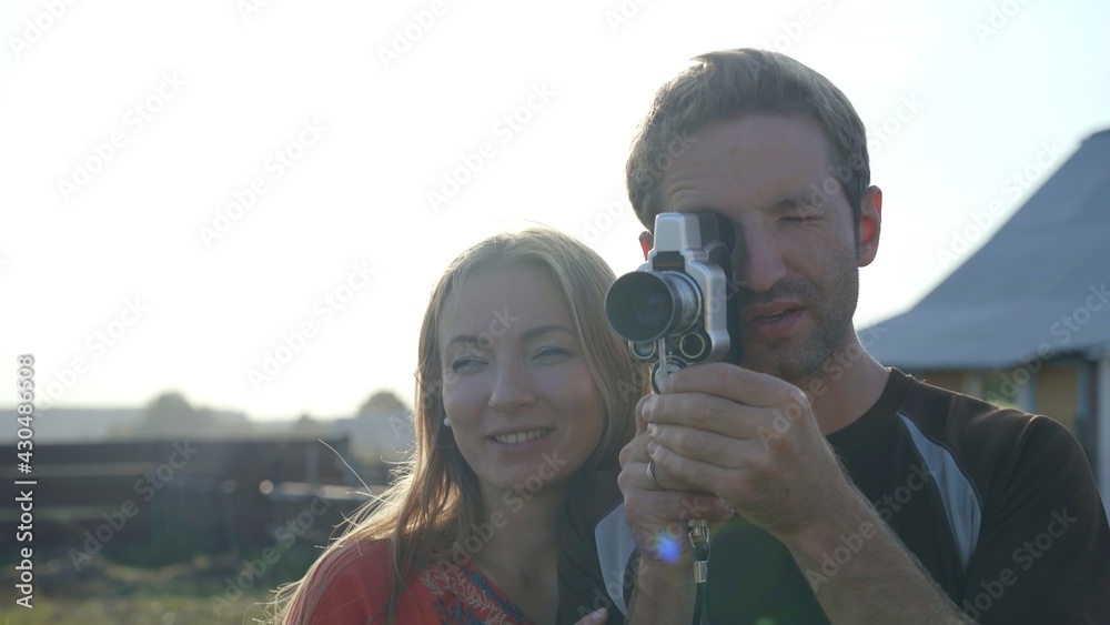 Fototapeta premium A young guy next to his girlfriend is filming a video on a retro video camera from the 60s.
